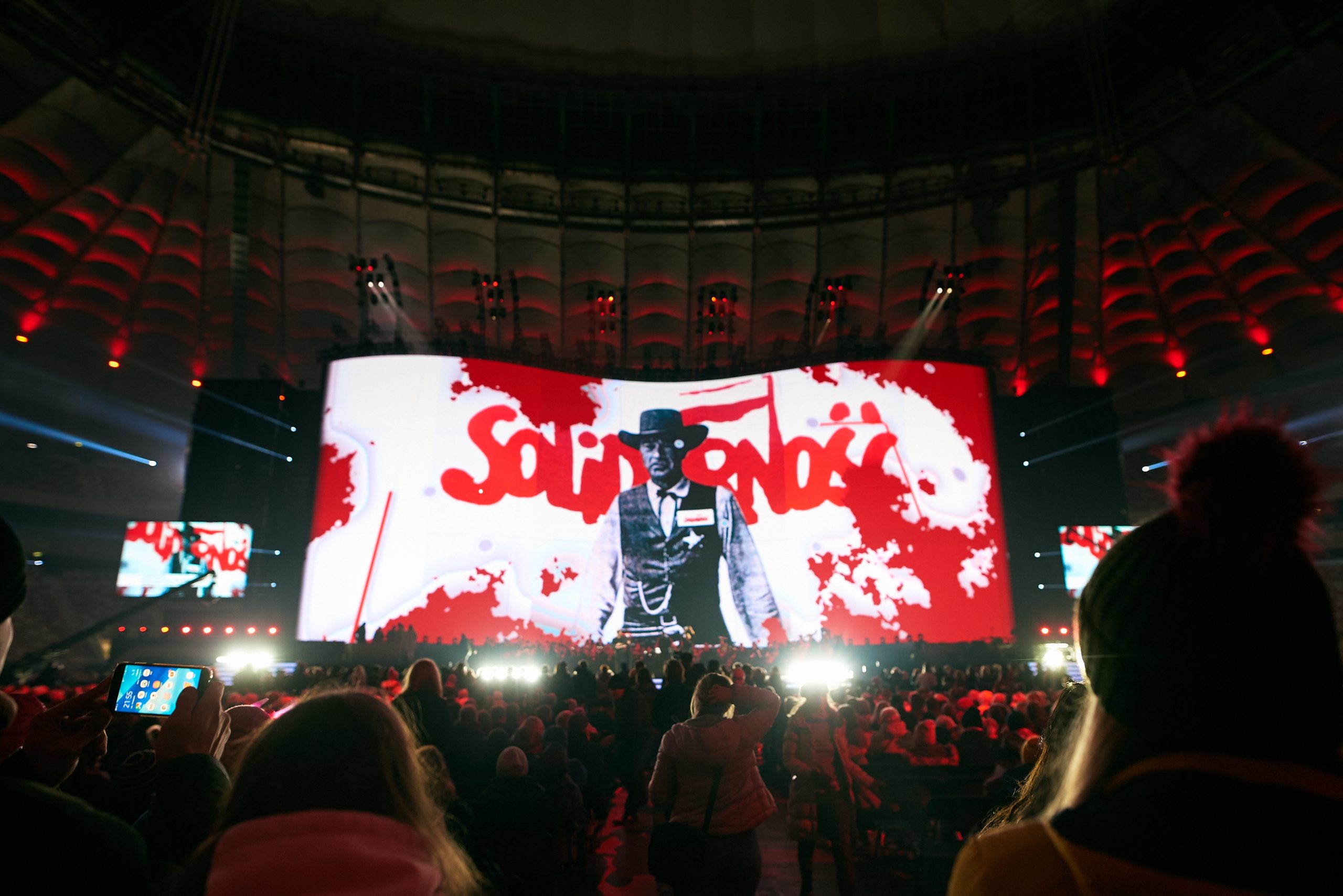 A photograph from the concert showing an outdoor screen with the “Solidarity” logo
