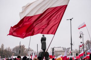 flagi trzymane przez ludzi pod pomnikiem Piłsudskiego