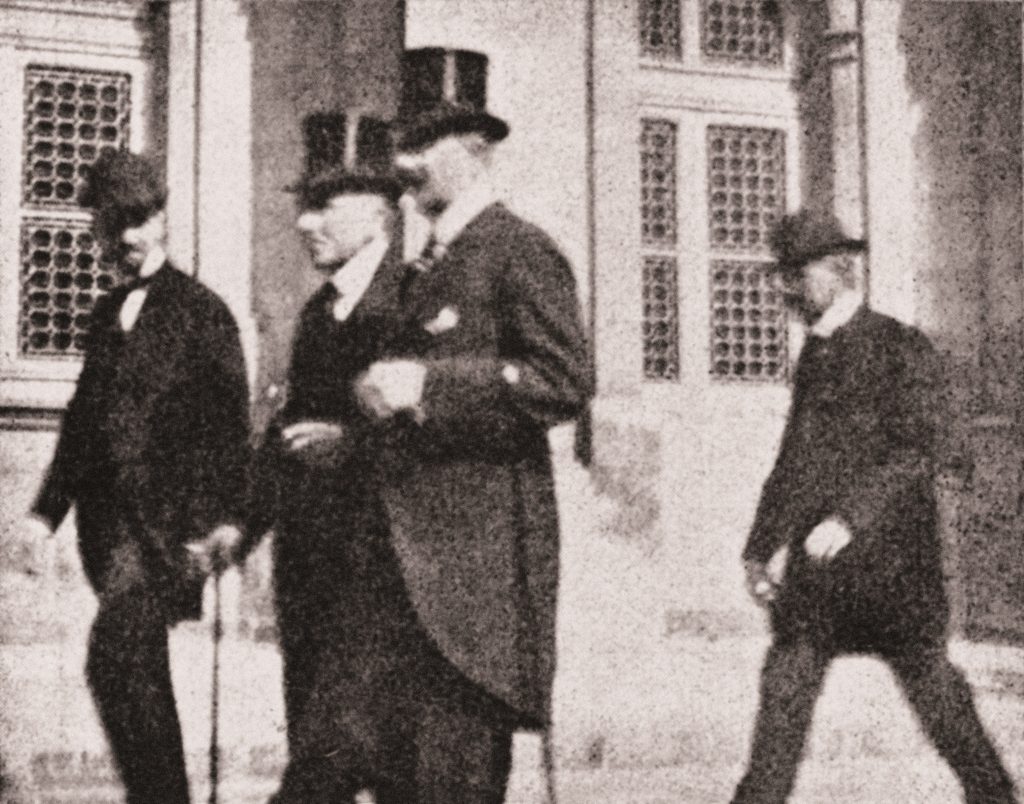 czterech mężczych w oficjalnych eleganckich strojach na ulicy, wśród nich: Roman Dmowski, hrabia Maurycy Zamoyski, Władysław Grabski