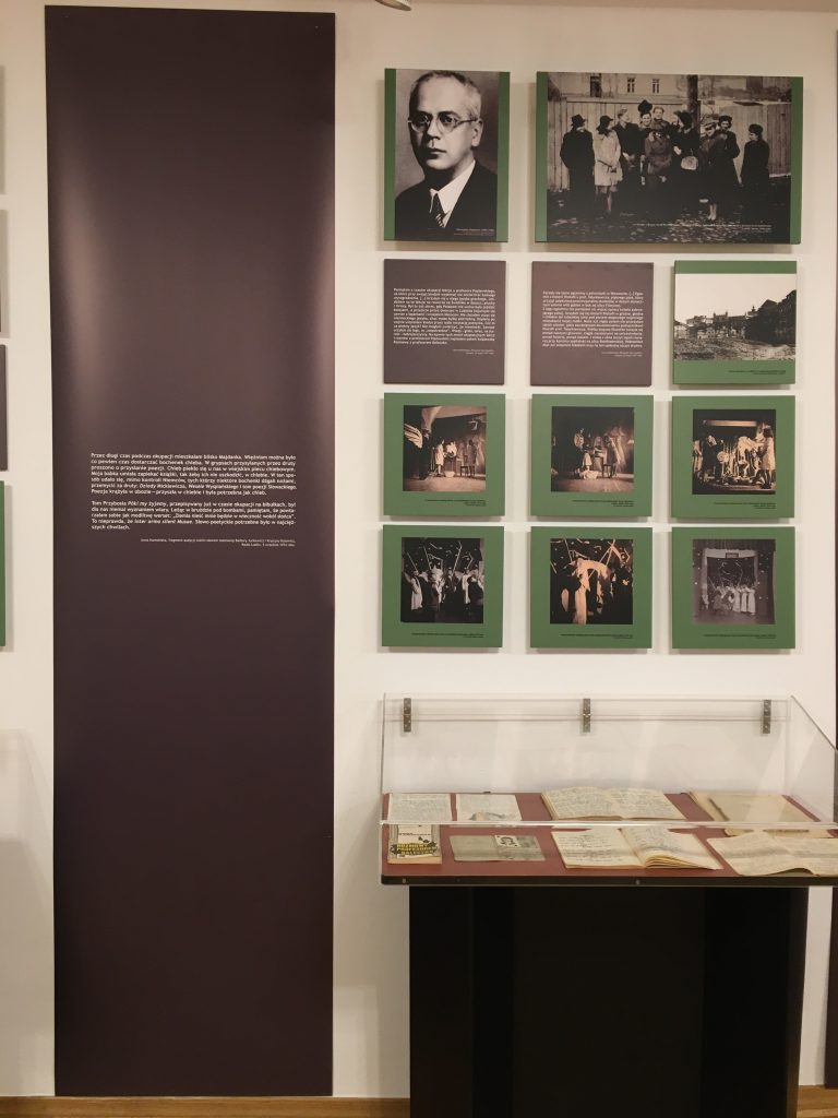 fragment wystawy - na ścianie zdjęcia, plansze i element ozdobny z cytatem, poniżej stoi witrynka z eksponatami