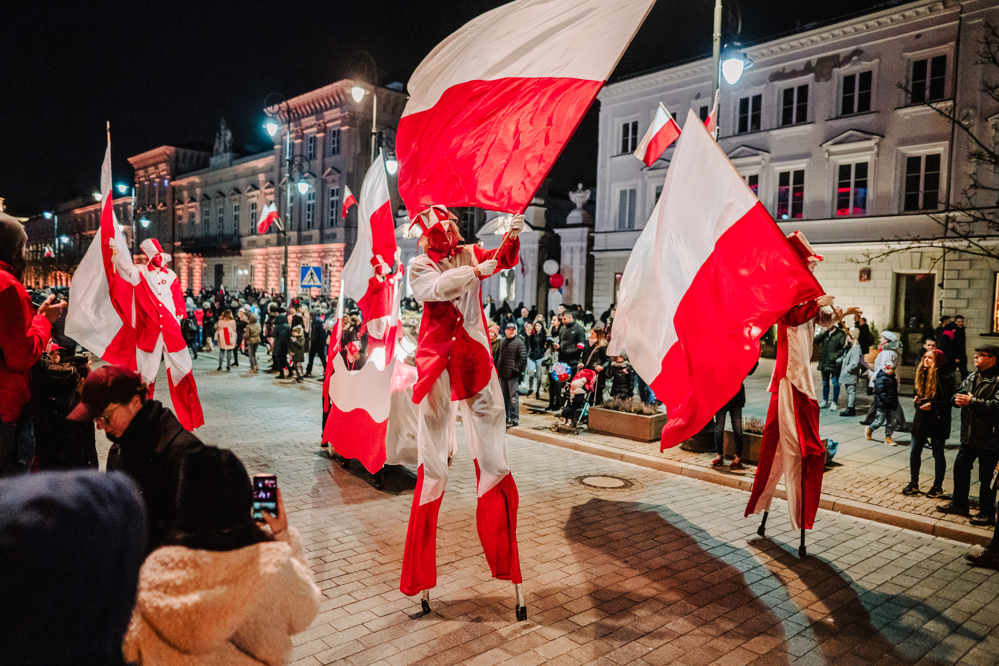 artyści na szczudłach z flagami Polski spacerują po krawkowskim przedmieściu