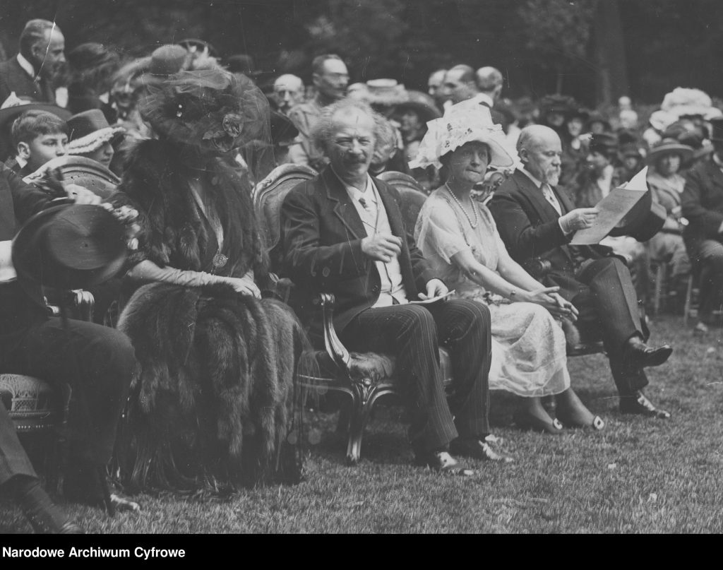 odświętnie ubrani ludzie na krzesłach na trawniku podczas uroczystości
