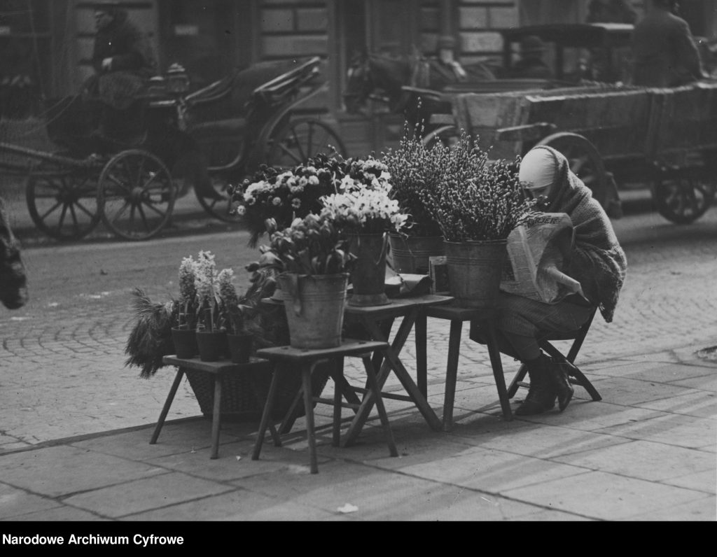 kwiaciarka ze swoim stoiskiem, czyta gazetę czekając na klientów