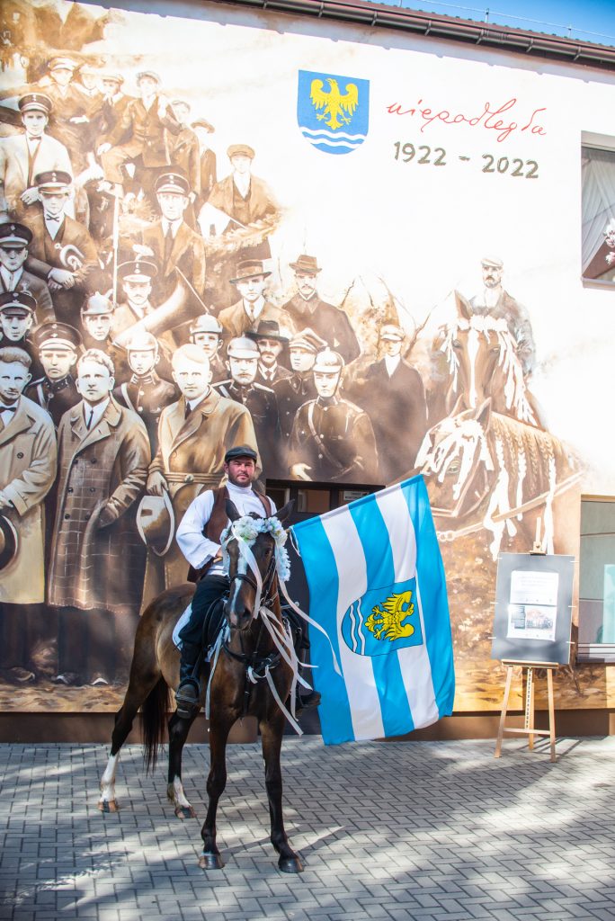 mężczyzna na koniu z rozwiniętą flagą pozuje przed muralem