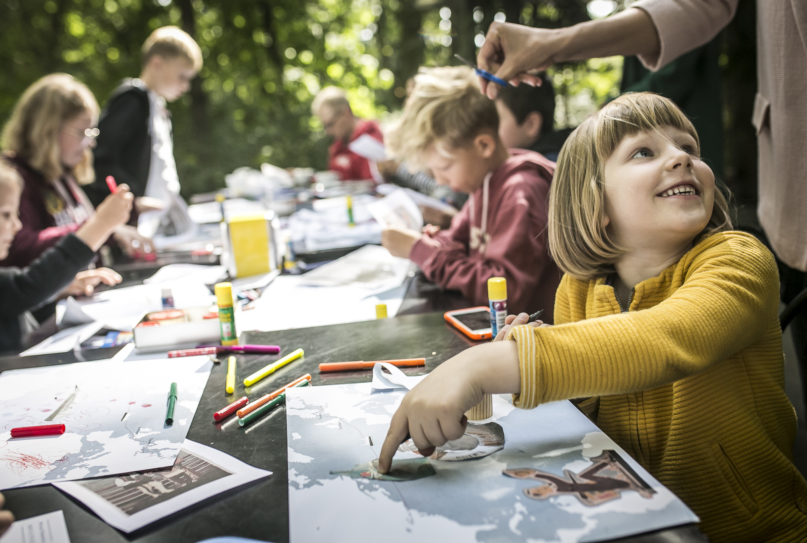 Zdjęcie przedstawia dzieci wykonujące prace plastyczne przy stole w ogródku pawilonu Niepodległa. Miejsce spotkań