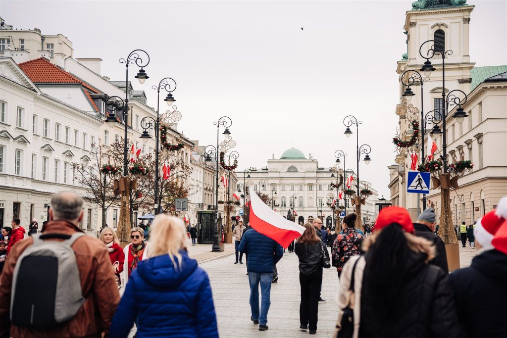 Krakowskie przedmieście, środkiem ulicy idzie mężczyzna z biało-czerwona flagą