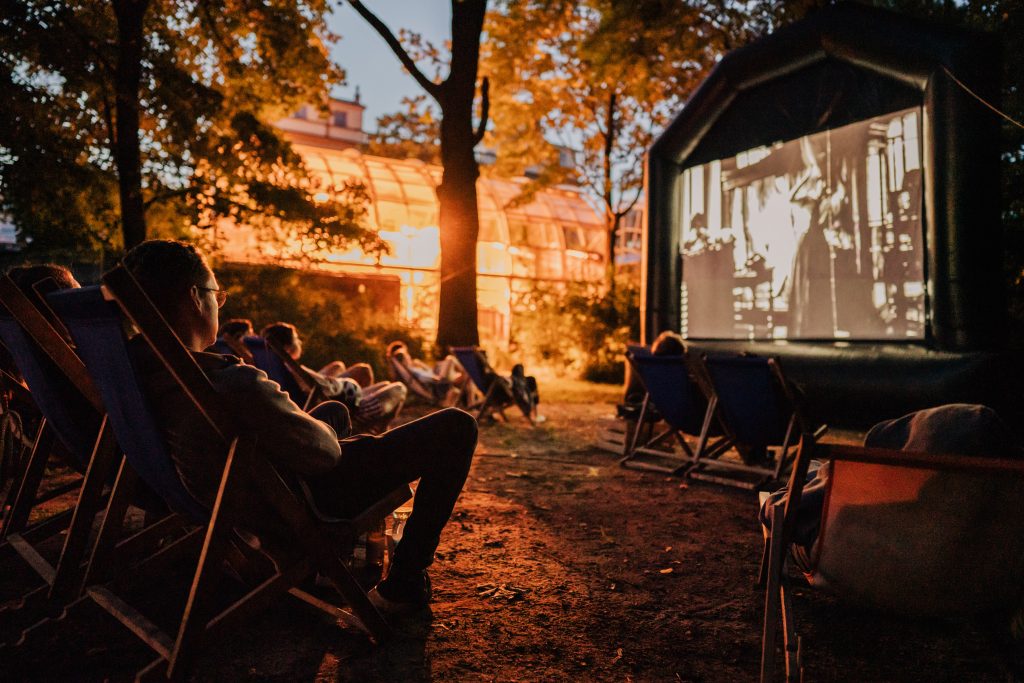 ludzie siedzą na leżakach, patrzą na ekran filmowy; zdjęcie po zmroku