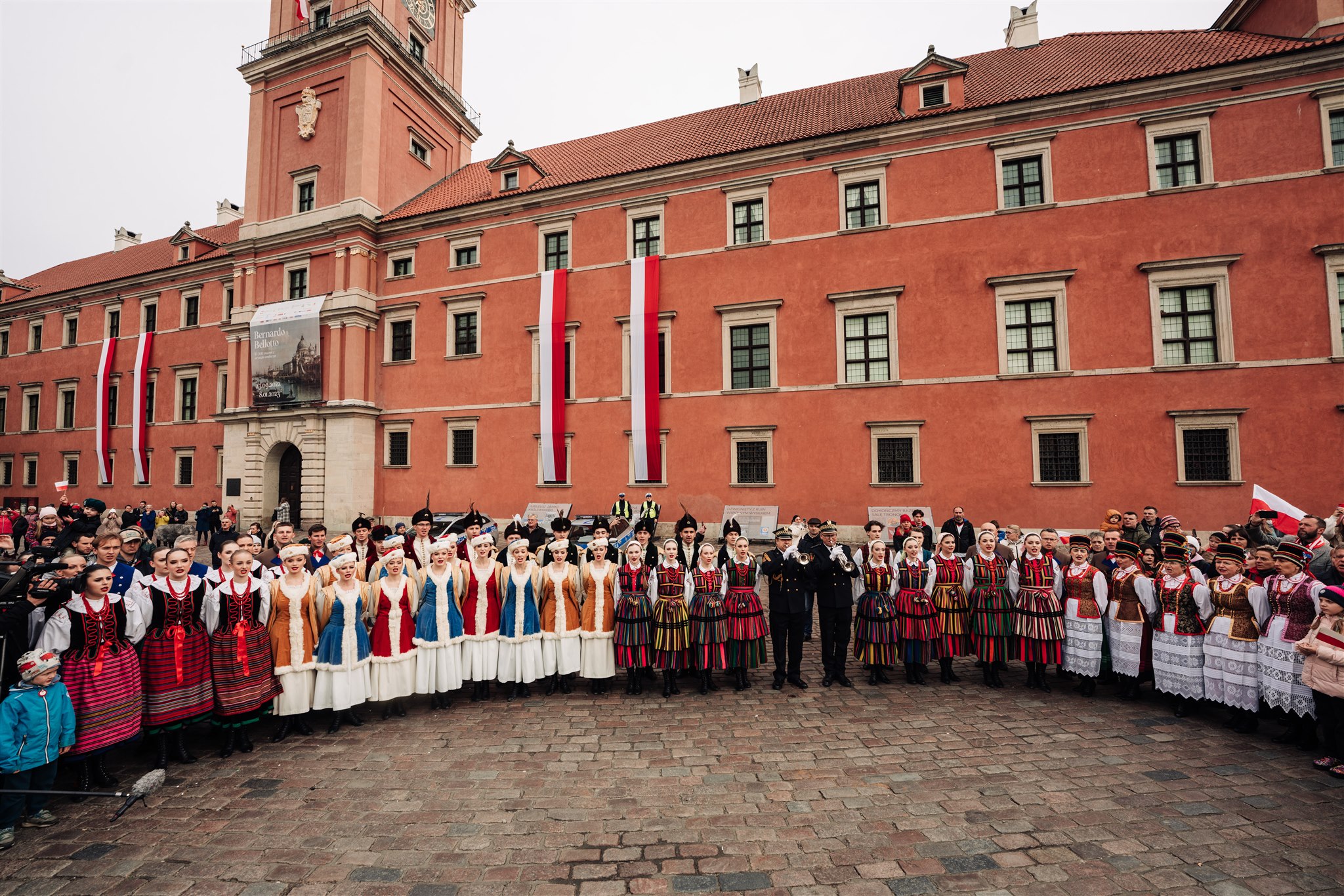 grupa ludzi śpiewa hymn pod zamkiem królewskim w Warszawie