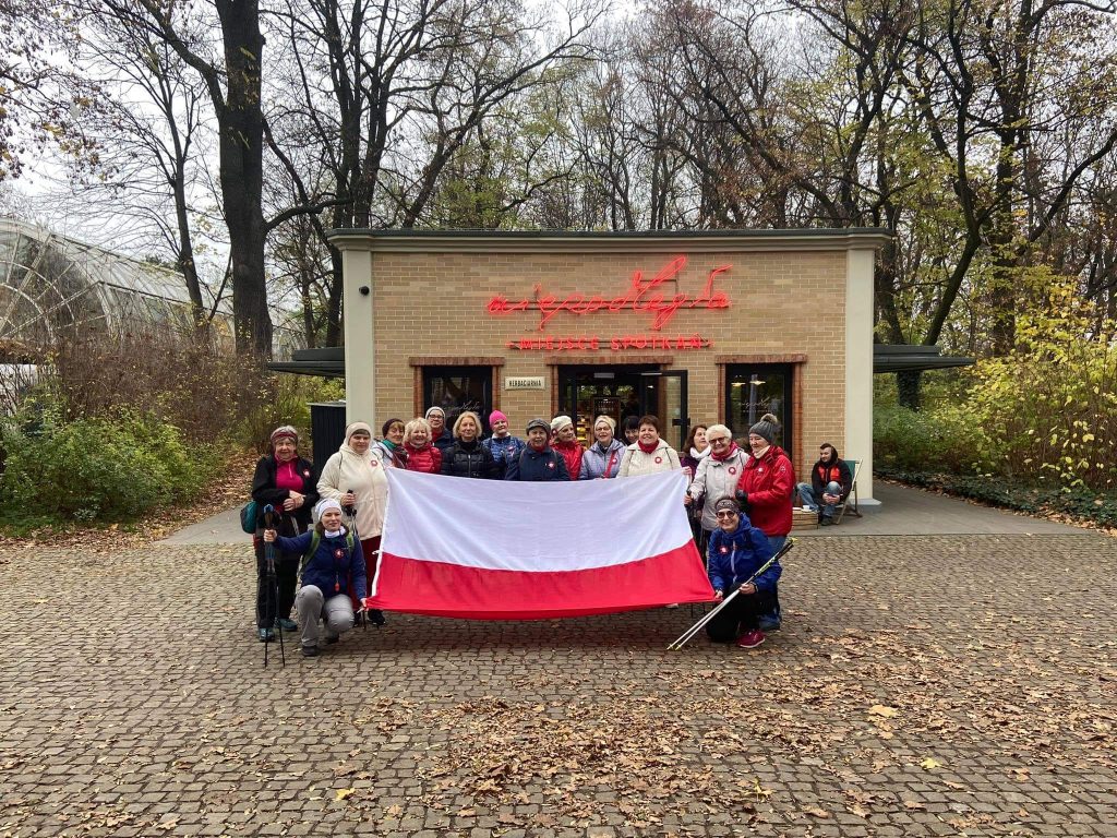 uczestniczki warsztatów z kijami nordic walking pozują z wielką flagą polski przed pawilonem niepodległa miejsce spotkań
