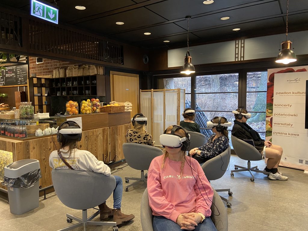 Zdjęcie przedstawia czworo uczestników pokazów filmów w technologii VR. Siedzą na obrotowych fotelach z goglami VR na twarzy.