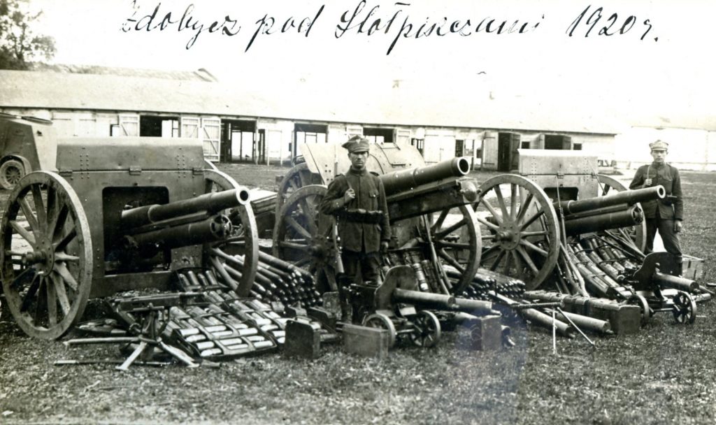 zdjęcie przedstawia żołnierzy 56 pułku piechoty Wielkopolskiej prezentujących zdobyte na bolszewikach w bitwie pod Stołpiszczem w dniu 4 czerwca 1920 r. armaty, ciężkie karabiny maszynowe i amunicję