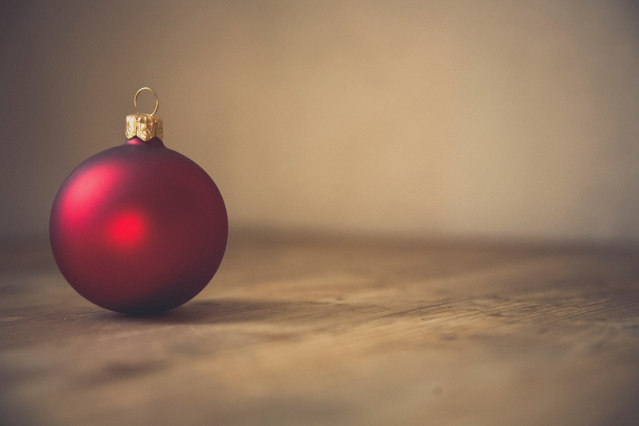 Zdjęcie przedstawia okrągłą bombkę świąteczną, która leży na drewnianym blacie.