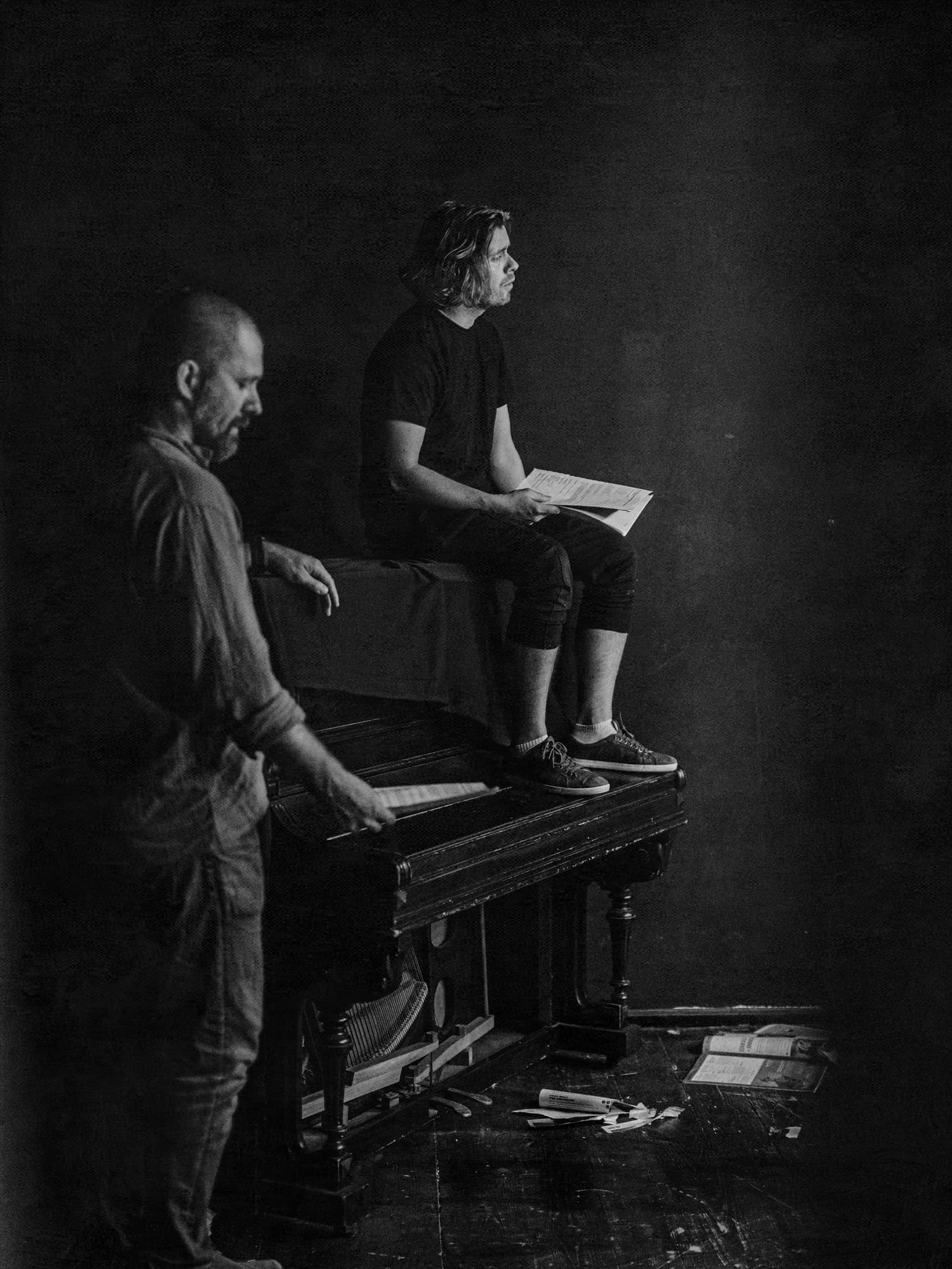 zdjęcei z próby, dwaj aktorzy na scenie, jeden klęczy przy pianinie, drugi stoi obok instrumentu
